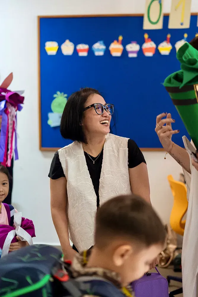A woman is standing in front of a group of children in a classroom.