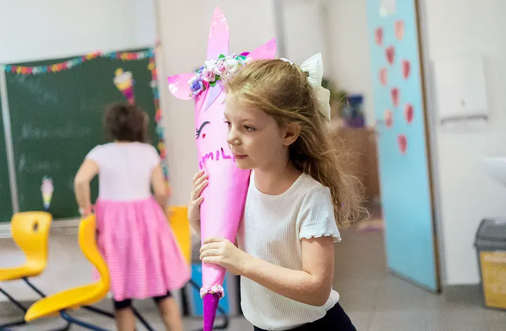 A little girl is holding a pink cone in a classroom.