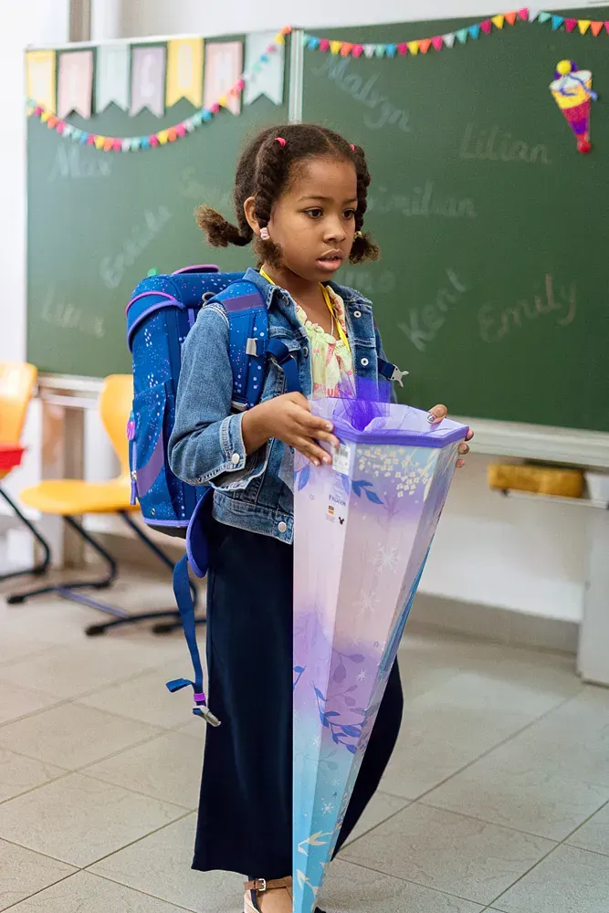 A little girl with a backpack is holding a cone in a classroom.