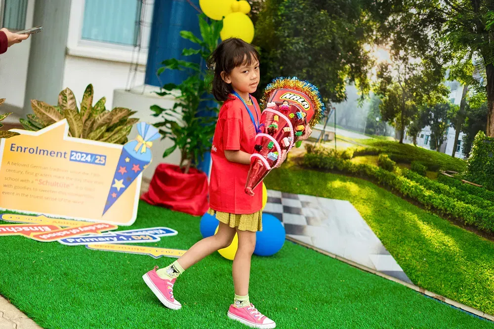 A little girl in a red shirt and pink shoes is walking on a green carpet.