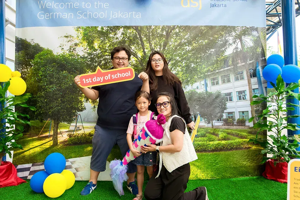 A family is posing for a picture in front of a sign that says `` welcome to the german school jakarta ''.