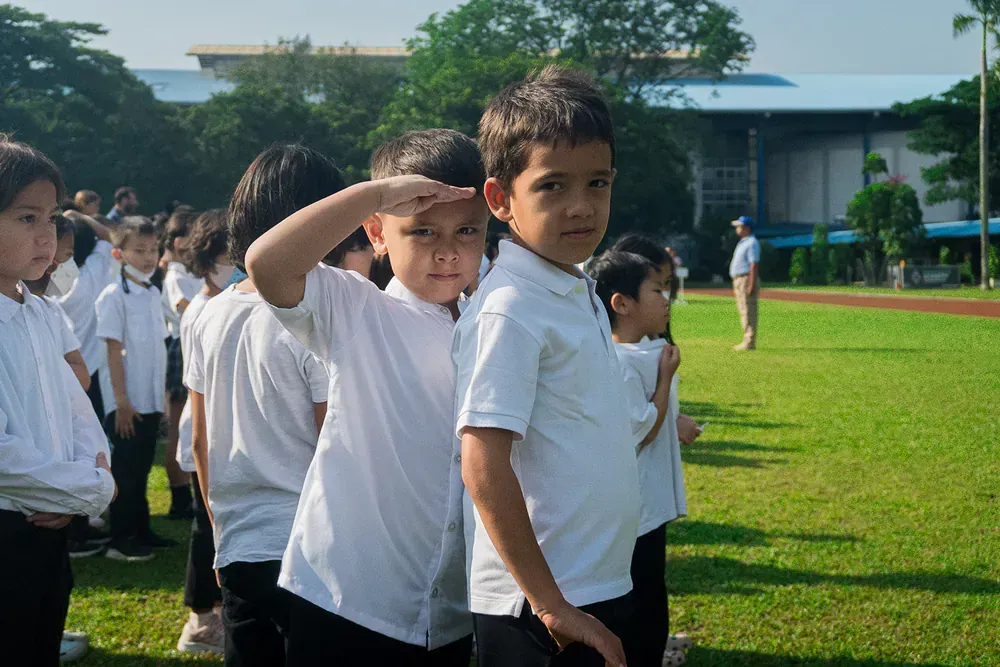 A group of children in white shirts are saluting in a field.