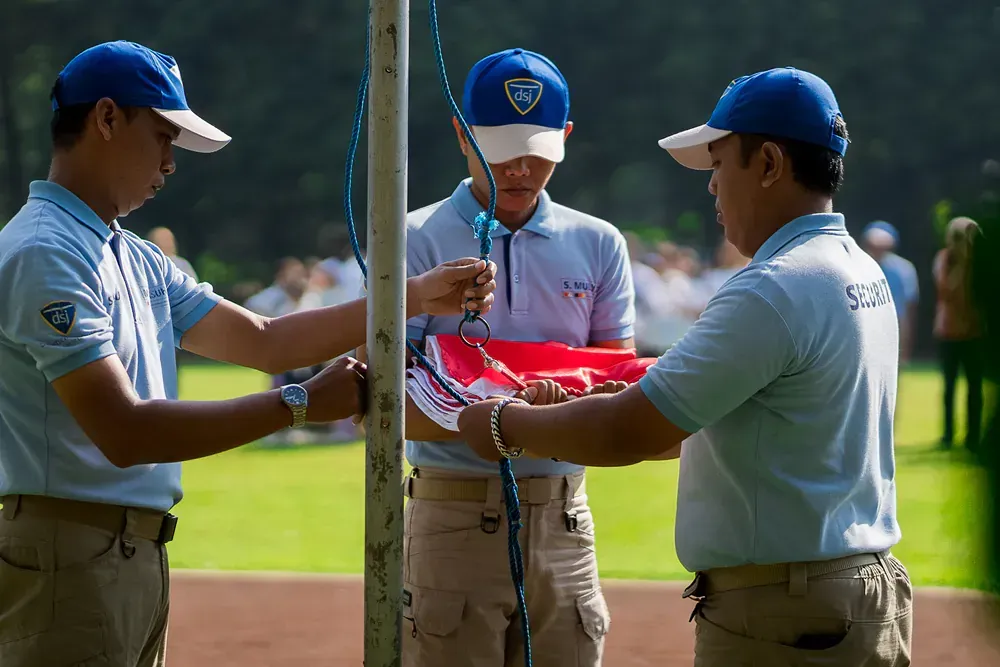 Three men in blue hats are standing around a pole