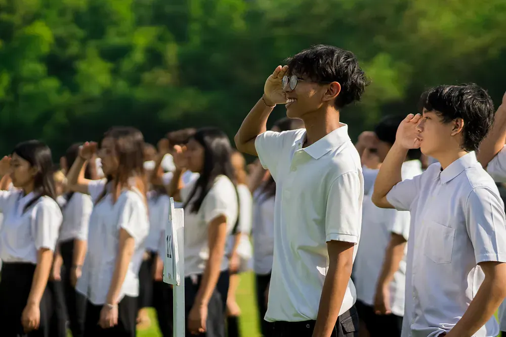 A group of young people in school uniforms are saluting in a field.