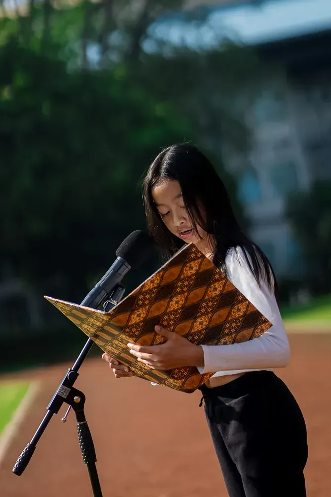 A woman is reading a book in front of a microphone.