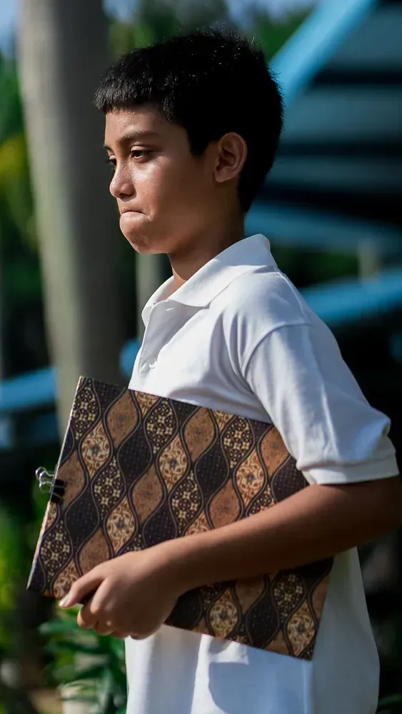 A young boy in a white shirt is holding a book.