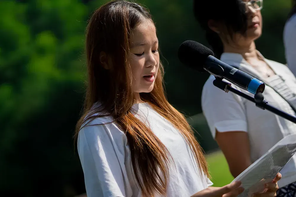 A young girl is singing into a microphone while holding a book.