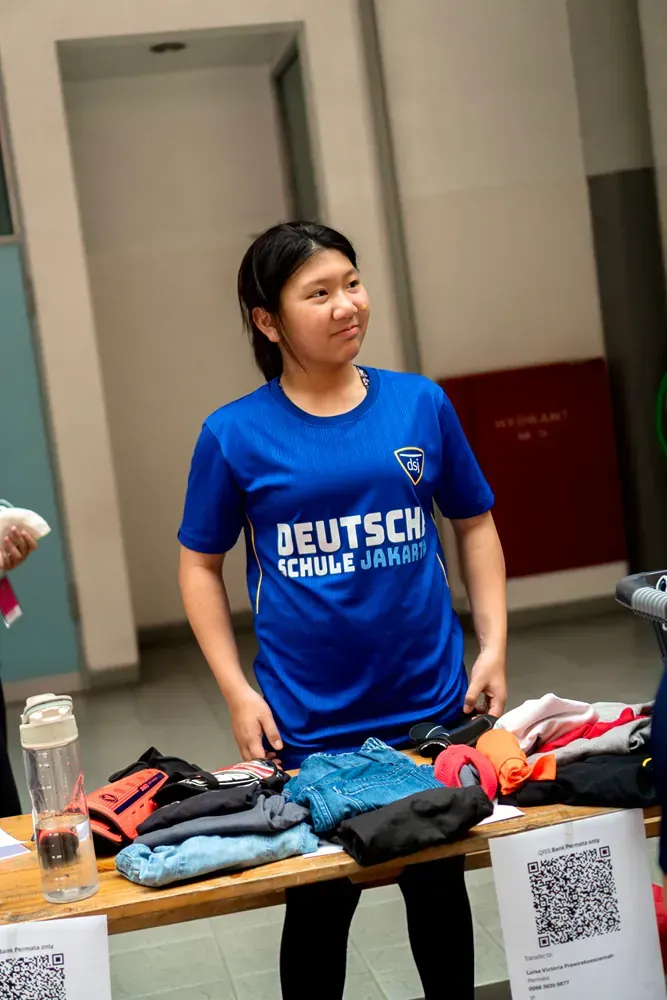 A woman in a blue shirt is standing in front of a table with clothes on it.