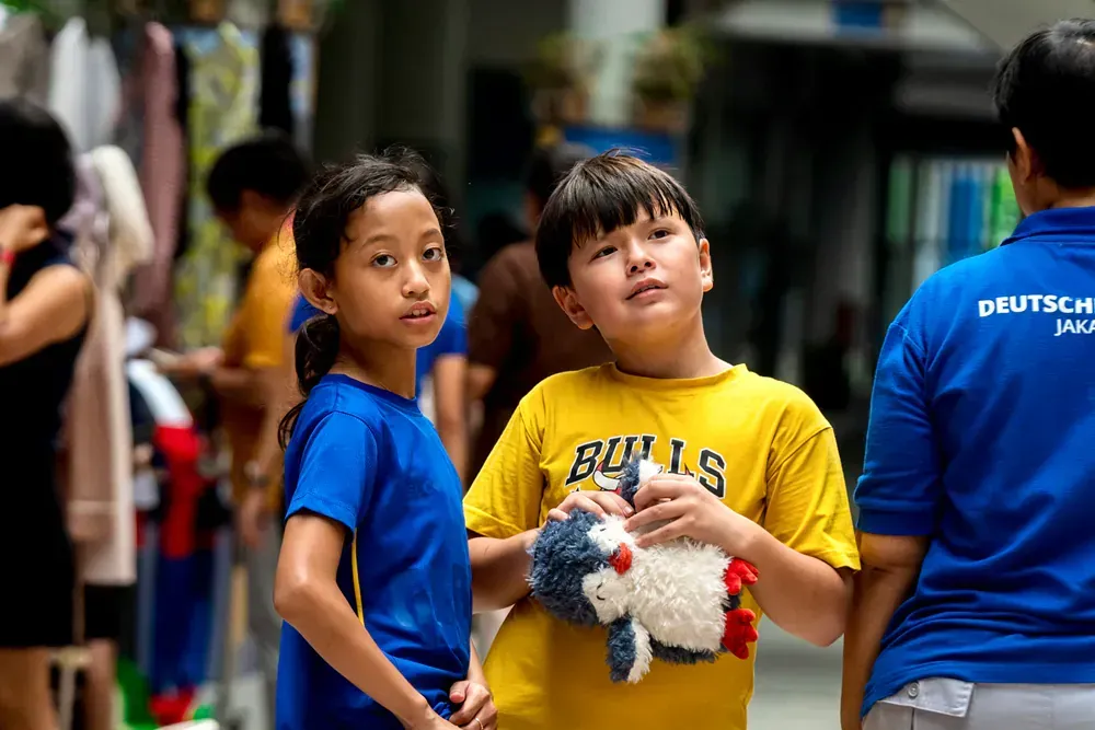 A boy in a yellow shirt is holding a stuffed animal next to a girl in a blue shirt.