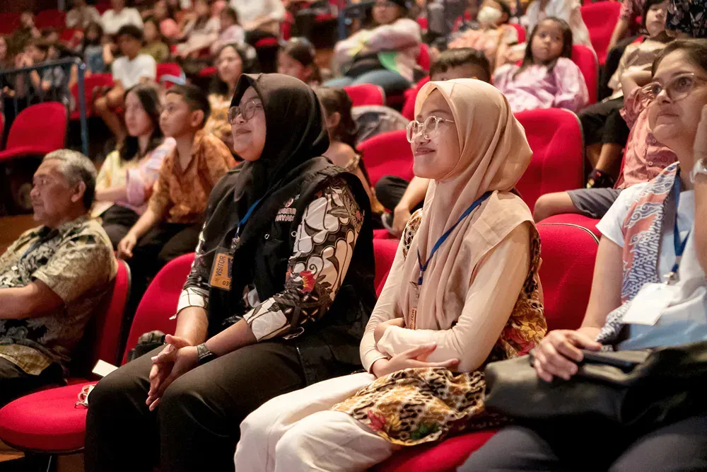 A group of people are sitting in red chairs in an auditorium.