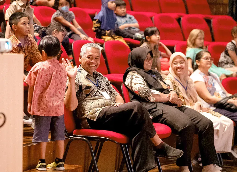 A group of people are sitting in red chairs in an auditorium.
