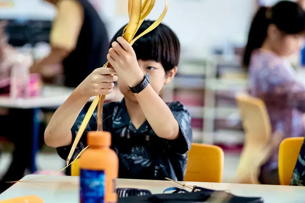 A young boy is sitting at a table in a classroom holding a yellow object.