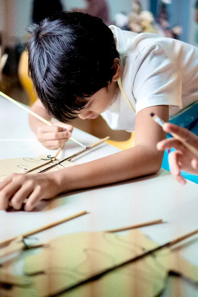 A young boy is sitting at a table painting with a brush.