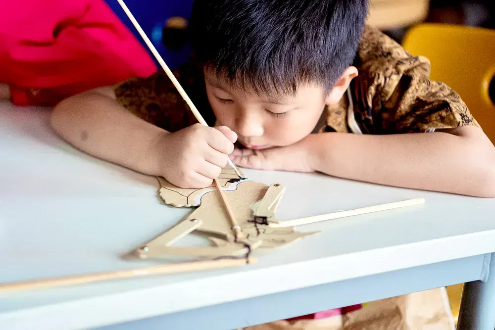 A young boy is sitting at a table playing with a wooden toy.