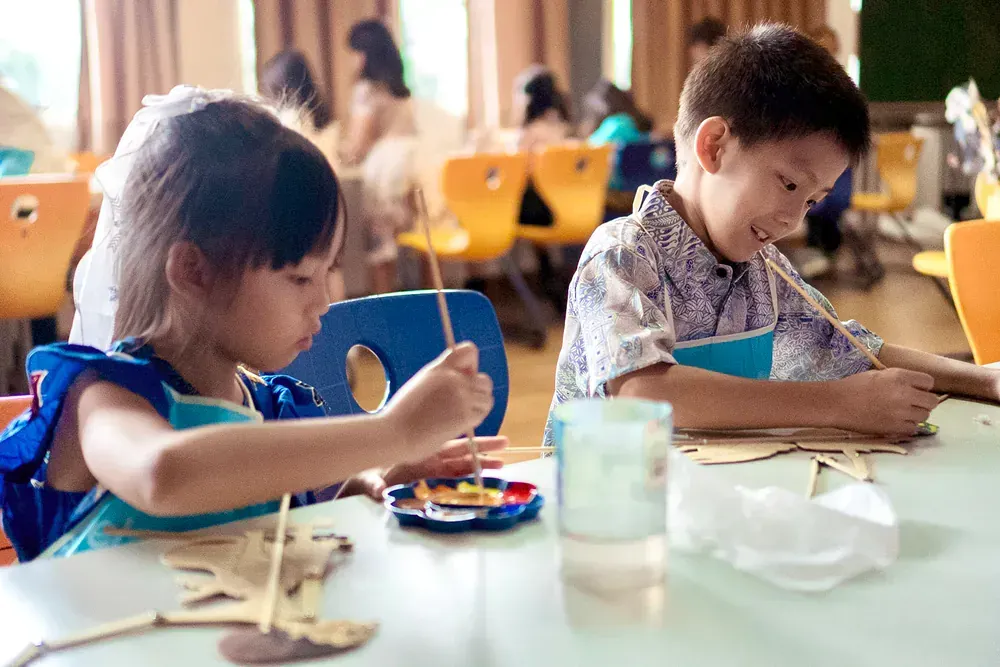 A boy and a girl are sitting at a table painting.