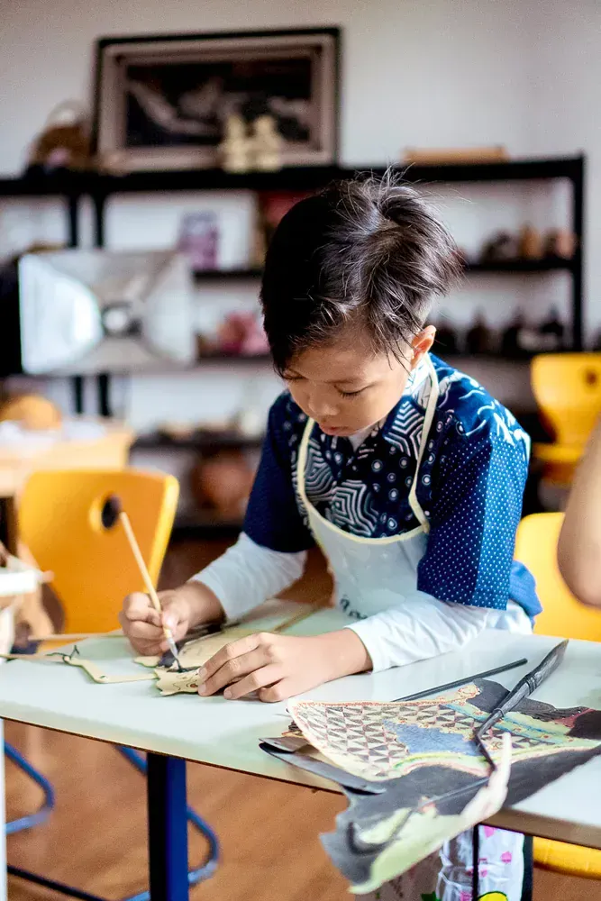 A young boy is sitting at a table painting with a brush.