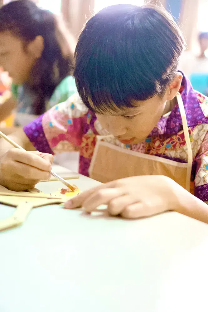 A young boy is sitting at a table painting with a brush.