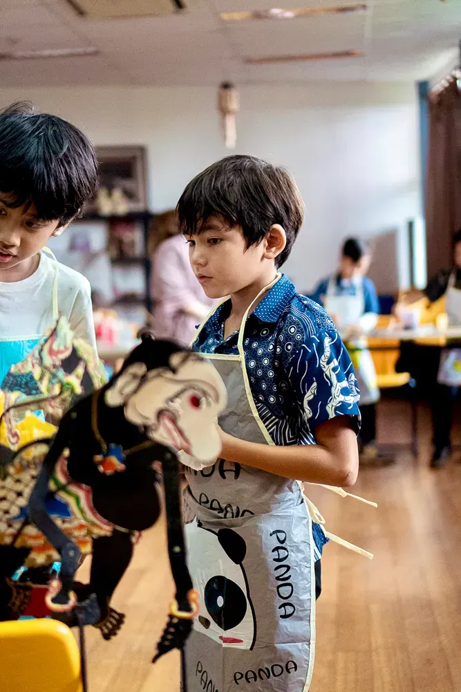 A young boy in an apron is holding a stuffed animal.
