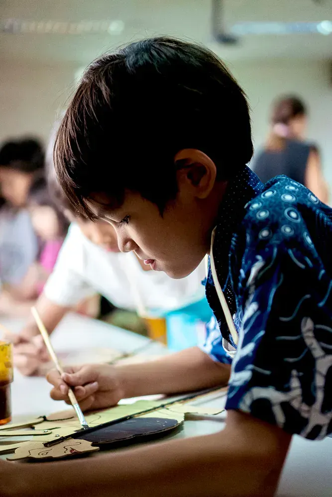 A young boy is sitting at a table painting with a brush.