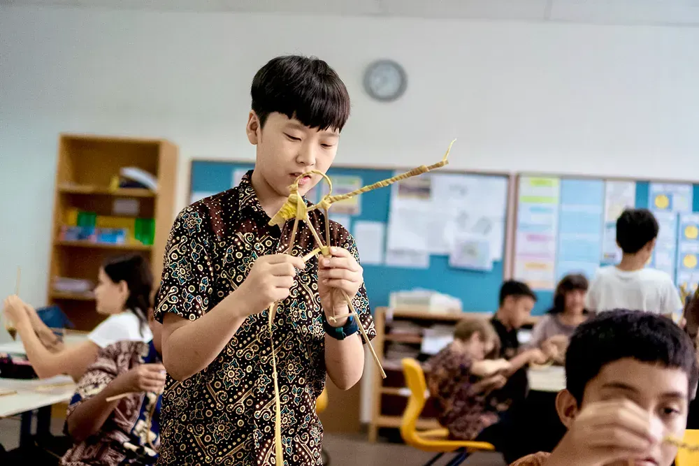 A young boy is holding a piece of wood in a classroom.