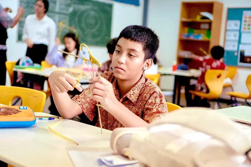 A young boy is sitting at a table in a classroom playing with a toy.