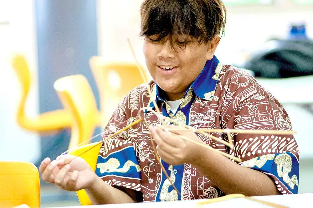 A young boy is sitting at a table playing with sticks.