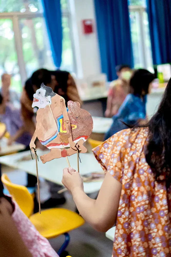 A girl is holding a puppet in her hand in a classroom.