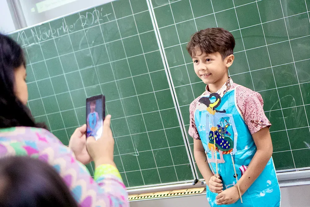 A woman is taking a picture of a young boy in front of a blackboard.