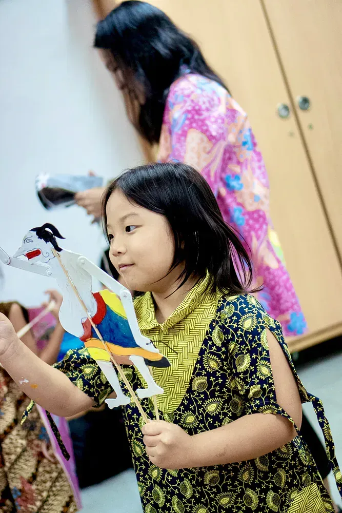 A little girl is holding a paper puppet while a woman looks on.