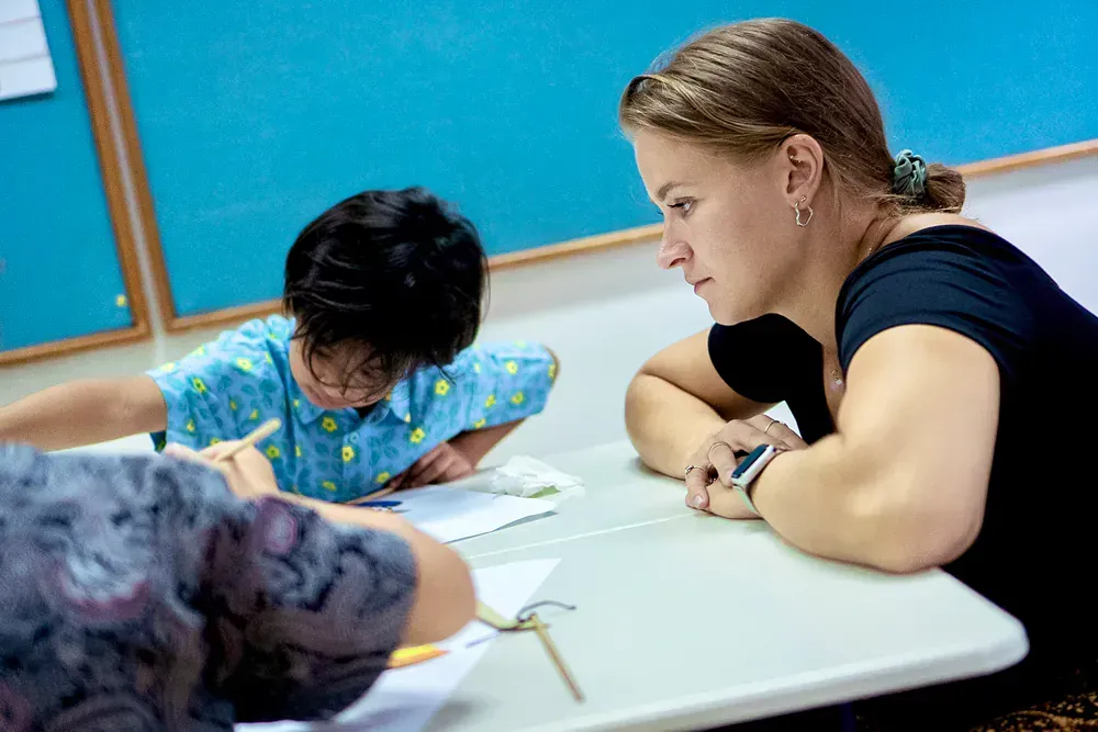 A woman is sitting at a desk with two children in a classroom.