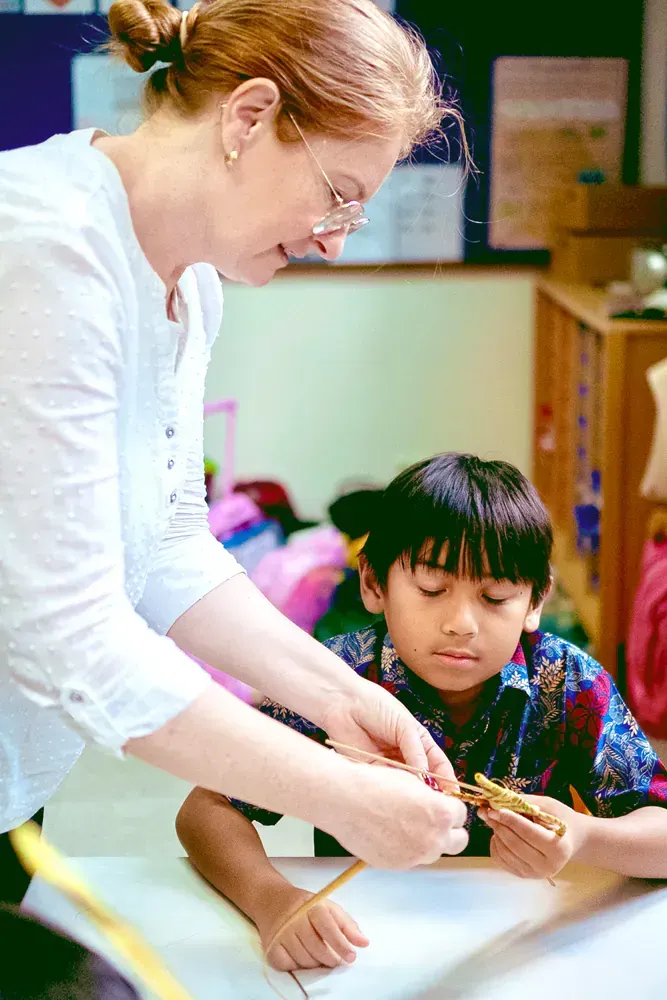 A teacher is helping a young boy with his homework in a classroom.