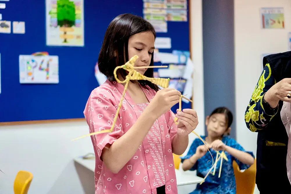 A girl in a pink shirt is holding a piece of spaghetti in her mouth.