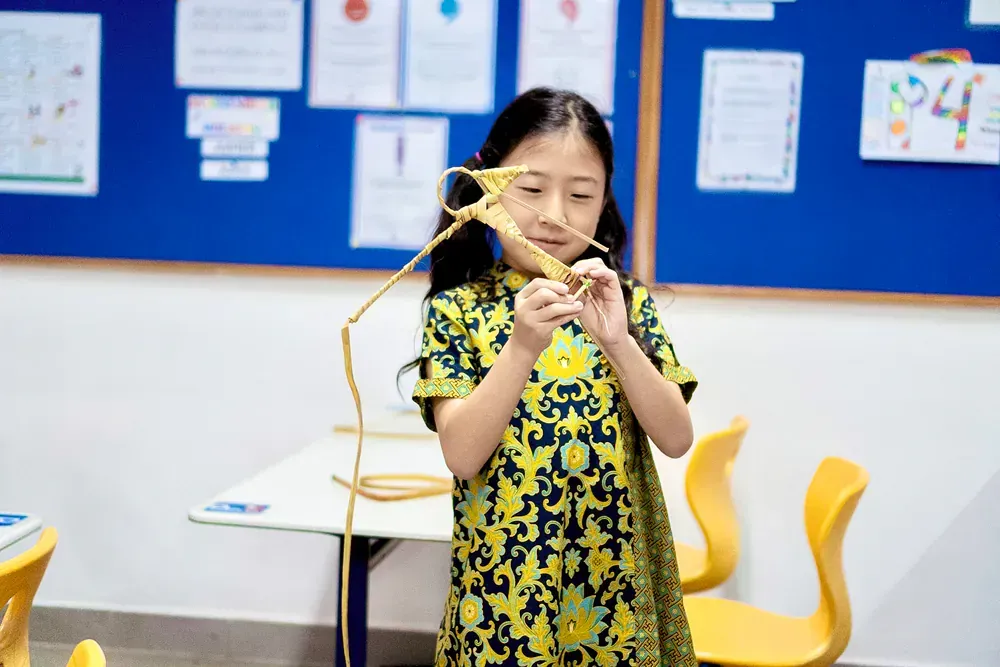 A young girl is holding a piece of wood in a classroom.
