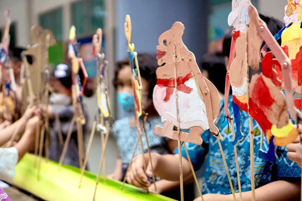A group of children are sitting at a table making paper puppets.