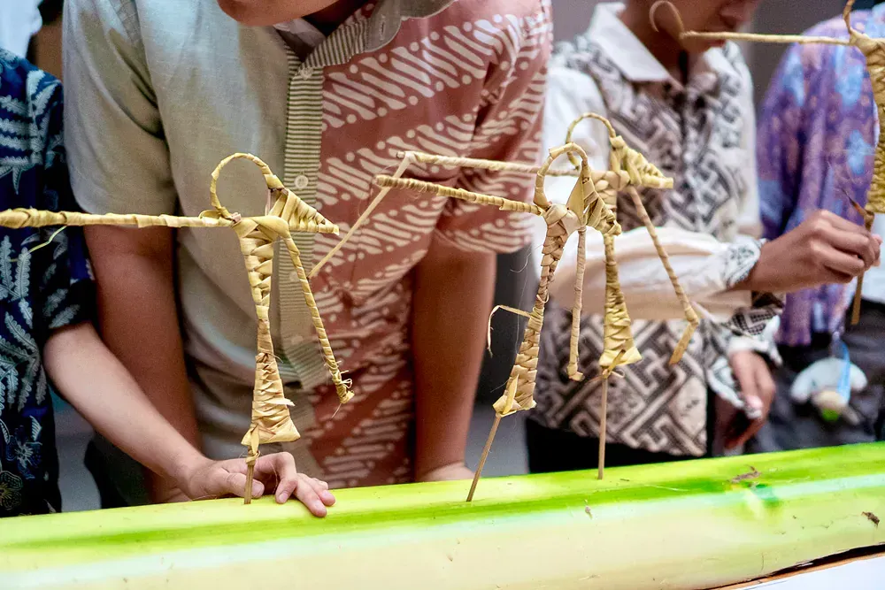 A group of people are looking at a sculpture of a grasshopper on a stick.