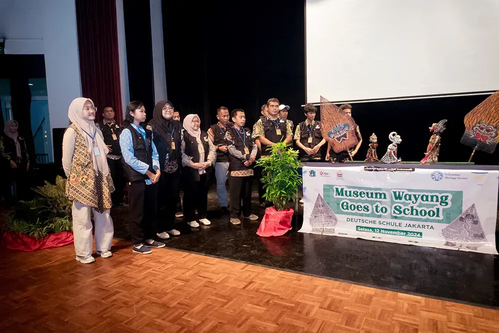 A group of people are standing on a stage in front of a sign that says museum wayang goes to school.