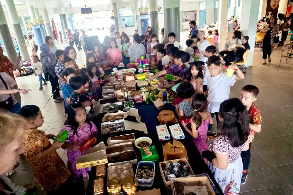 A large group of children are standing around a table filled with food.