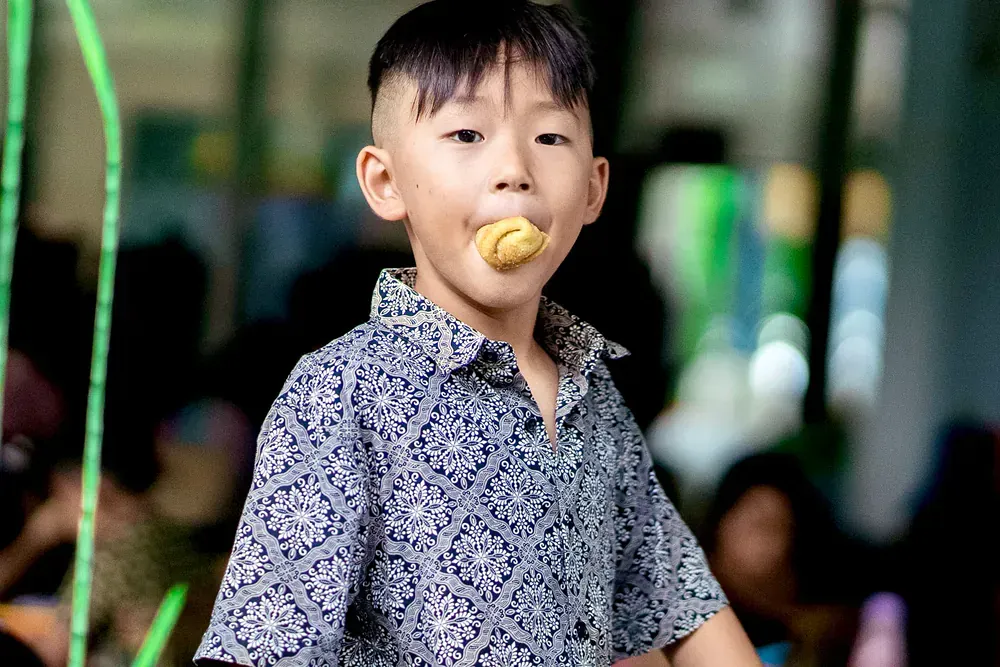 A young boy in a floral shirt is eating a cookie.