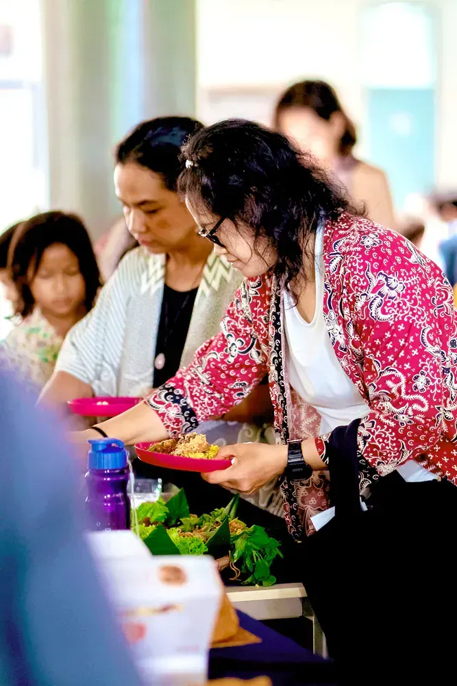 A woman in a pink jacket is reaching for a plate of food.