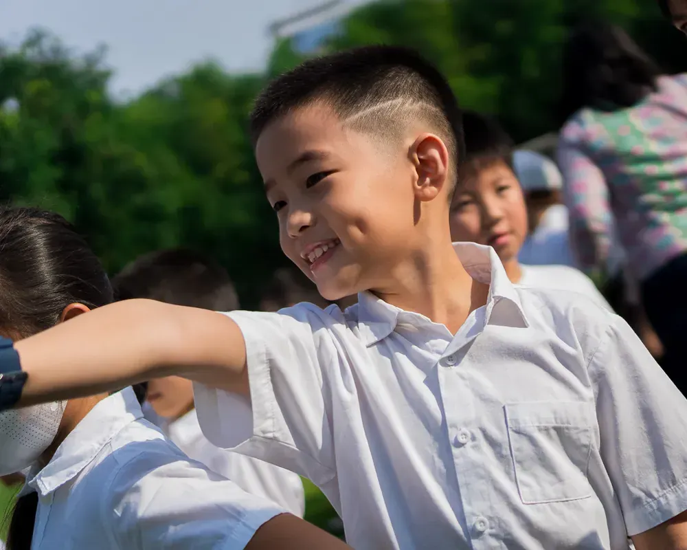 A young boy in a white shirt is standing in front of a group of children.