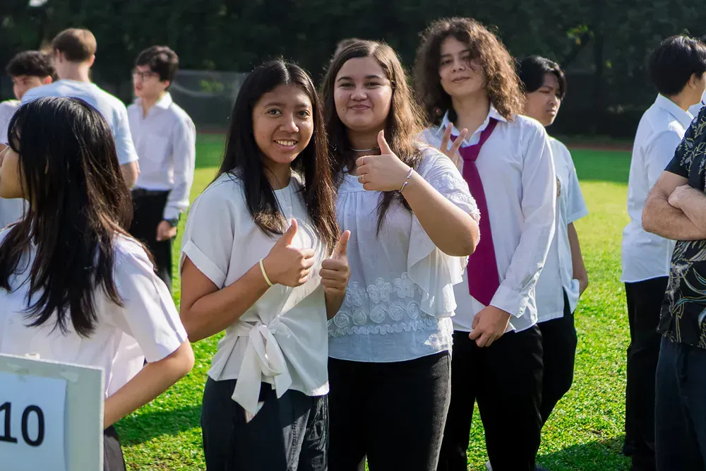 A group of people are standing in a line and one girl is giving a thumbs up