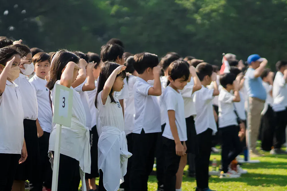 A group of children in school uniforms are saluting in a field.