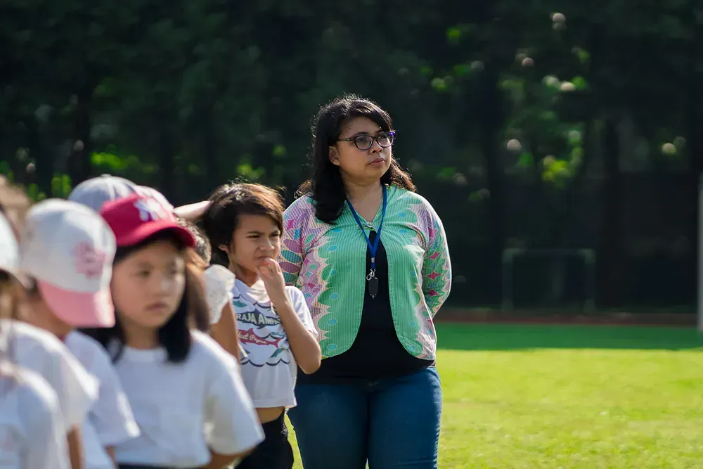 A woman is standing next to a group of children on a field.