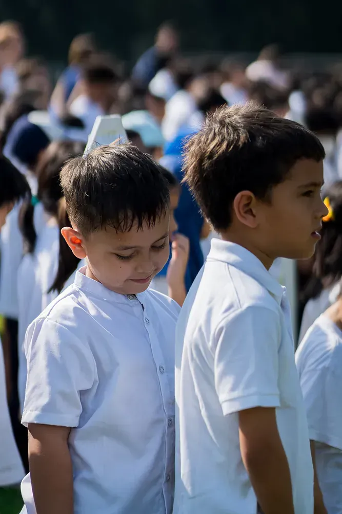 Two young boys are standing next to each other in a crowd of children.