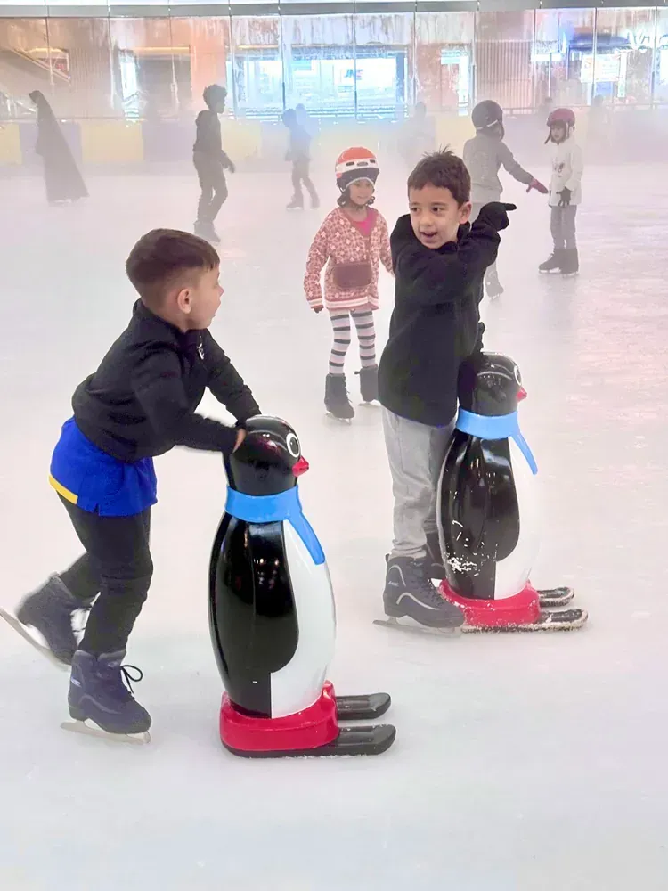A group of children are ice skating on a rink.