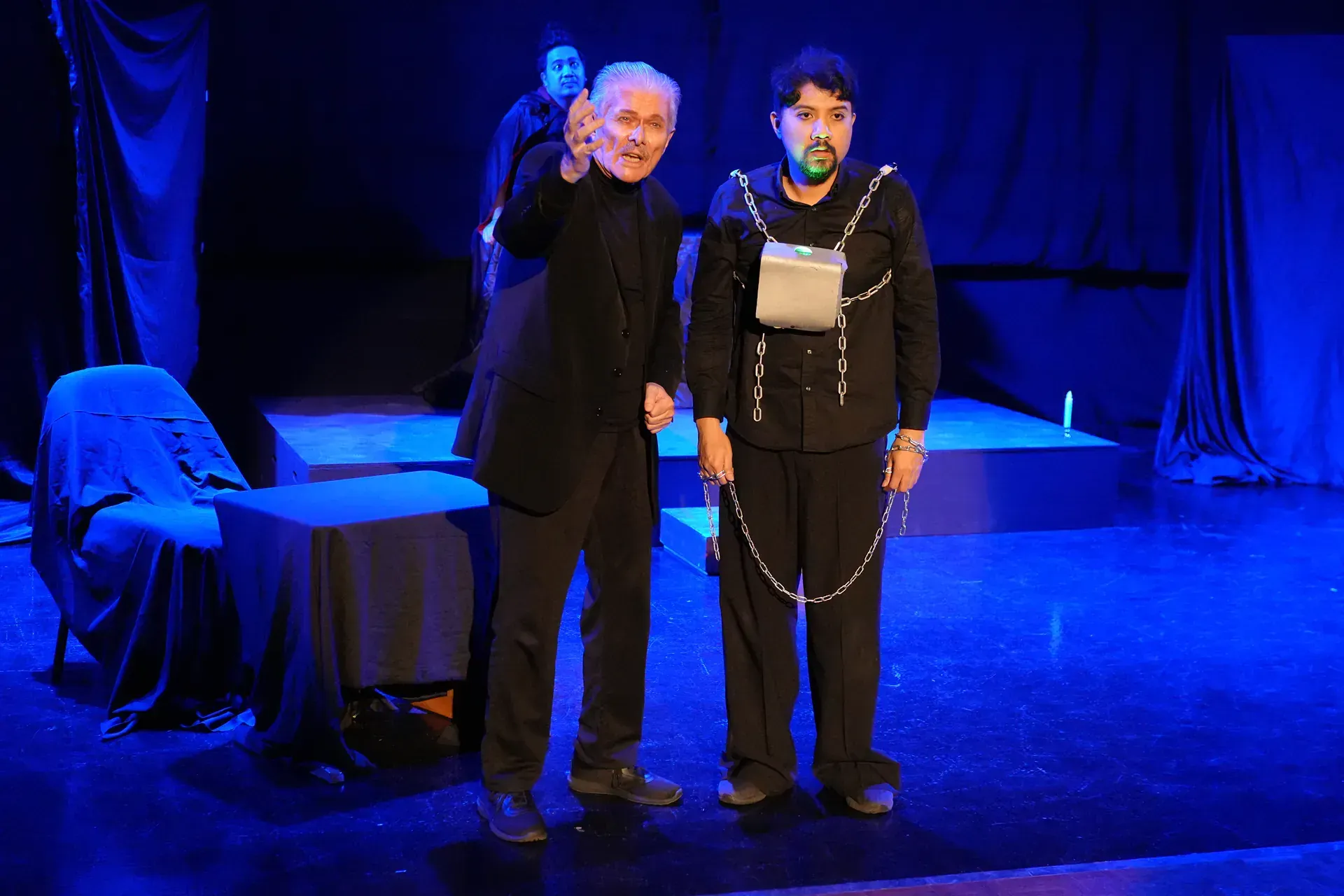 Two men are standing on a stage with a blue light behind them.