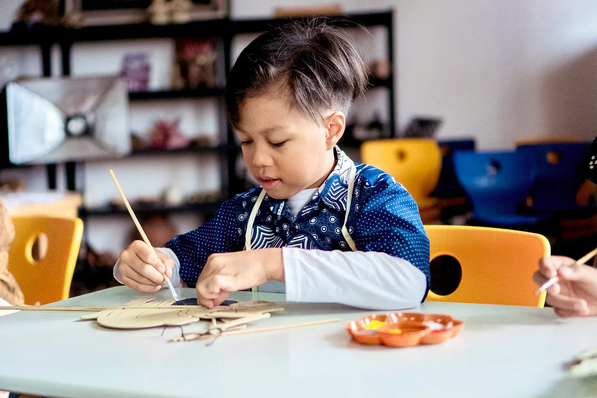 A young boy is sitting at a table painting with a brush.