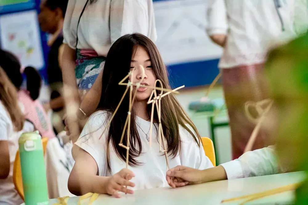 A girl is sitting at a table with a bunch of sticks in her hair.