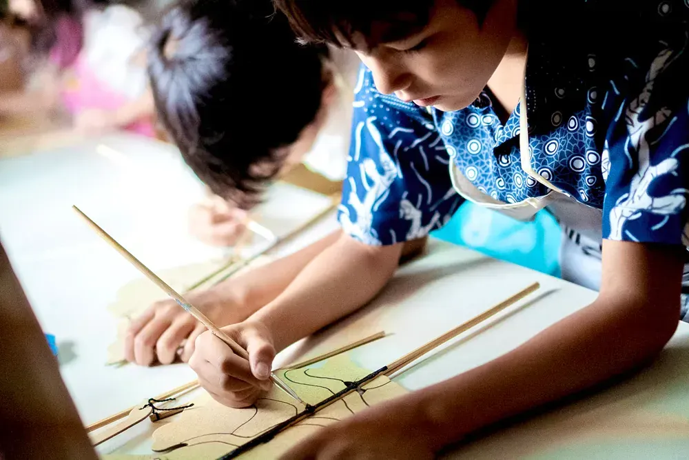 A group of children are sitting at a table drawing on a piece of paper.