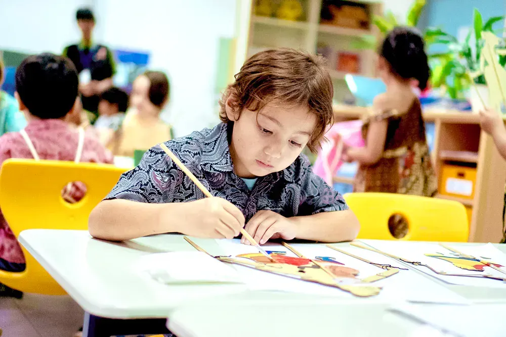 A young boy is sitting at a table painting with a brush.
